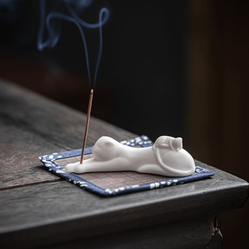 White ceramic cat incense holder in lounging pose, curling smoke on navy mat