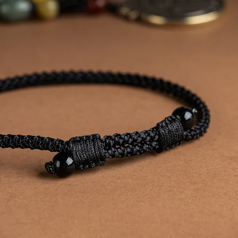 12 Chinese Zodiac Fortune Necklace Pendant – Black woven cord bracelet with polished obsidian beads secured by wrapped knots, adjustable sliding closure, close-up macro detail on warm brown textured background, spiritual protection bracelet