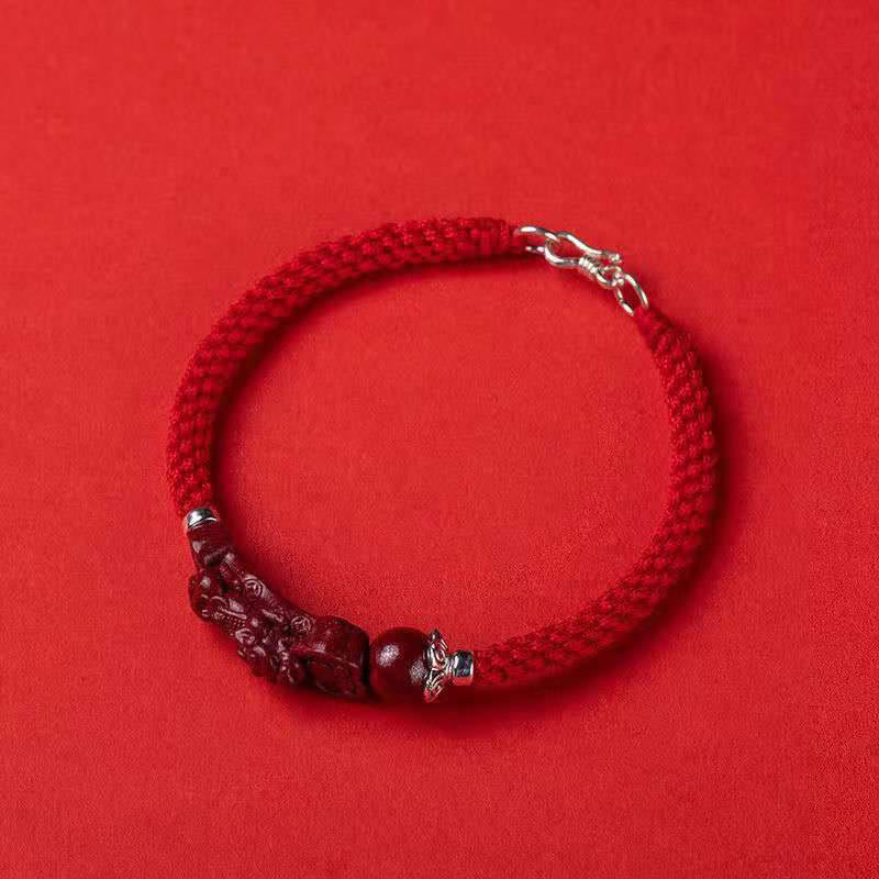 Handcrafted PiXiu Cinnabar Wealth Luck Braided Bracelet – top down flat lay on red surface, product photography