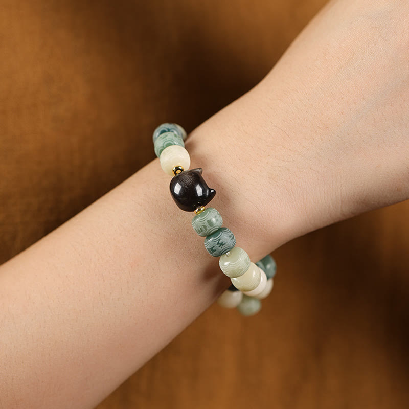 Bodhi Seed Cat Head Bracelet – Worn on wrist over wooden surface, green and cream beads with black cat charm focal point, healing bracelet