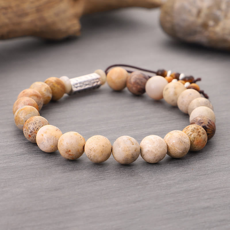 Weathered Stone Om Mani Padme Hum Bracelet – fossil coral beads with Tibetan script charm on gray surface, grounding
