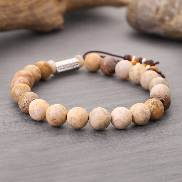 Weathered Stone Om Mani Padme Hum Bracelet – fossil coral beads with Tibetan script charm on gray surface, grounding