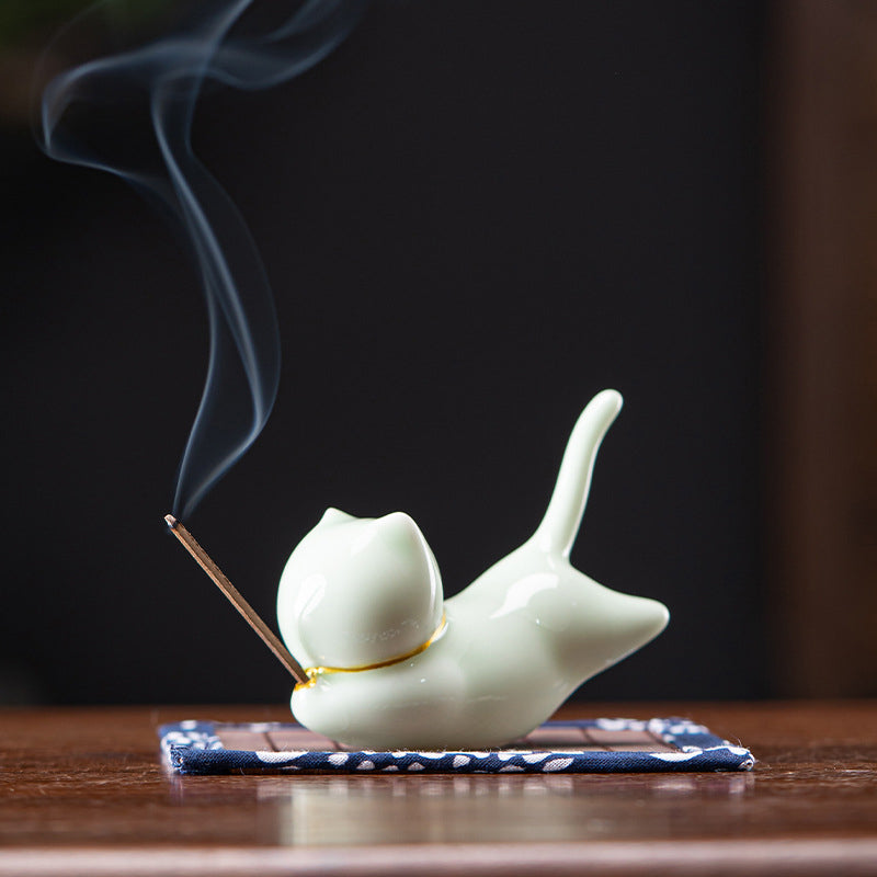 Celadon green ceramic cat incense holder with gold collar, smoke on blue mat