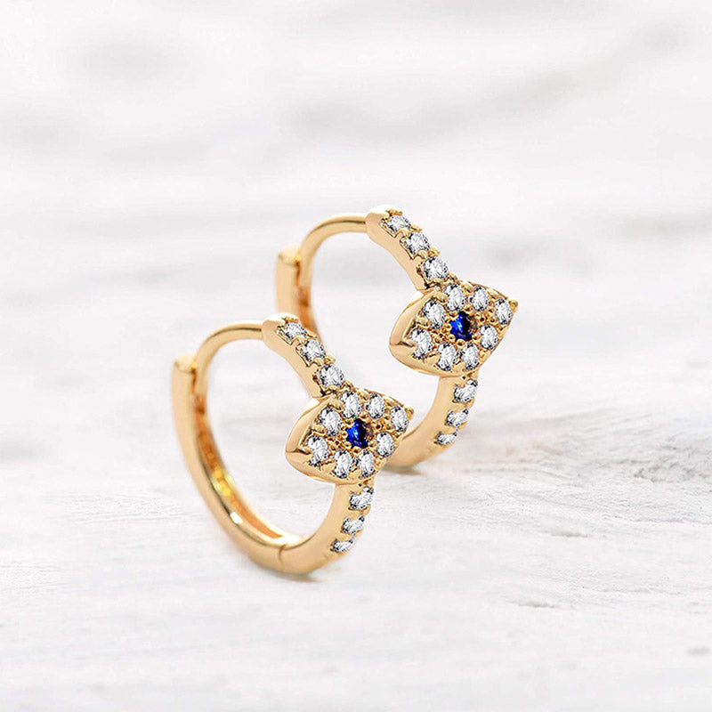 Evil Eye Stud Earrings – Gold evil eye huggie hoops with blue sapphire, on white wood surface