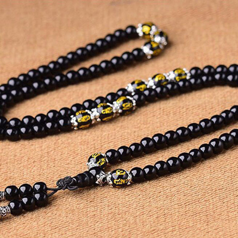 Black Obsidian Mala Bracelet - Flat lay S-curve showing gold-inscribed accent beads and tassel detail, obsidian prayer beads