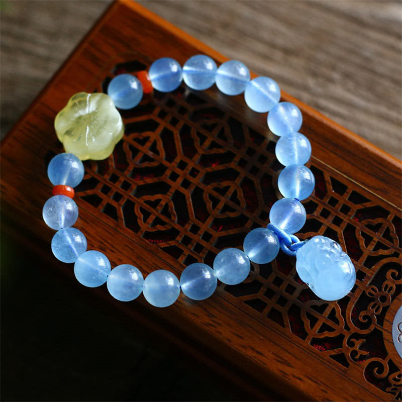 Aquamarine PiXiu Bracelet – Blue bead bracelet with carved yellow flower on wooden tray, healing jewelry