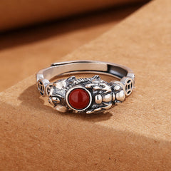 PiXiu Red Agate Wealth Ring on brown textured paper, carved guardian creature, coin band detail, feng shui