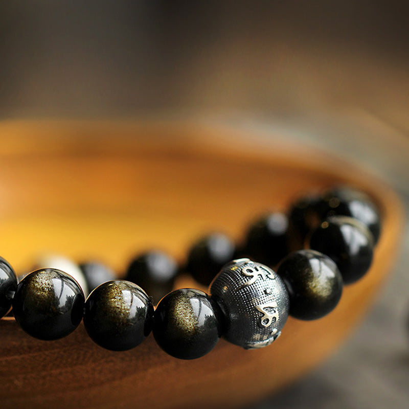 Zodiac Natal Buddha Obsidian Silver Bracelet - Macro of carved silver mantra bead on polished wood surface