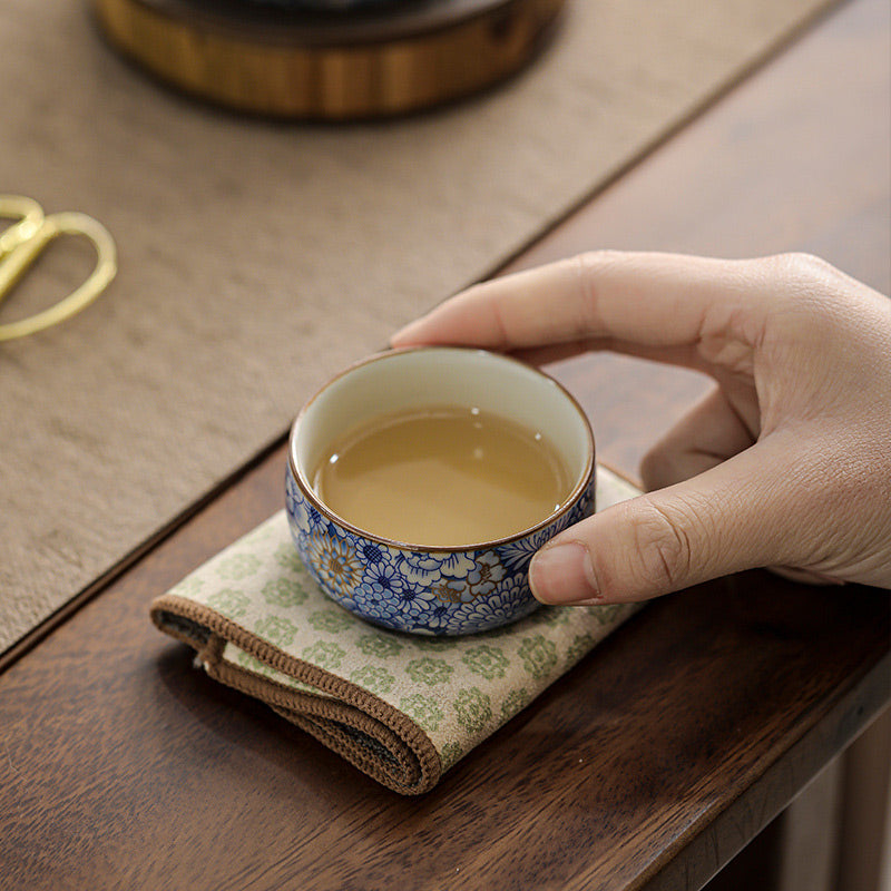 Lotus Chrysanthemum Ceramic Tea Cup - Blue cup with tea on green cloth, authentic tea setting