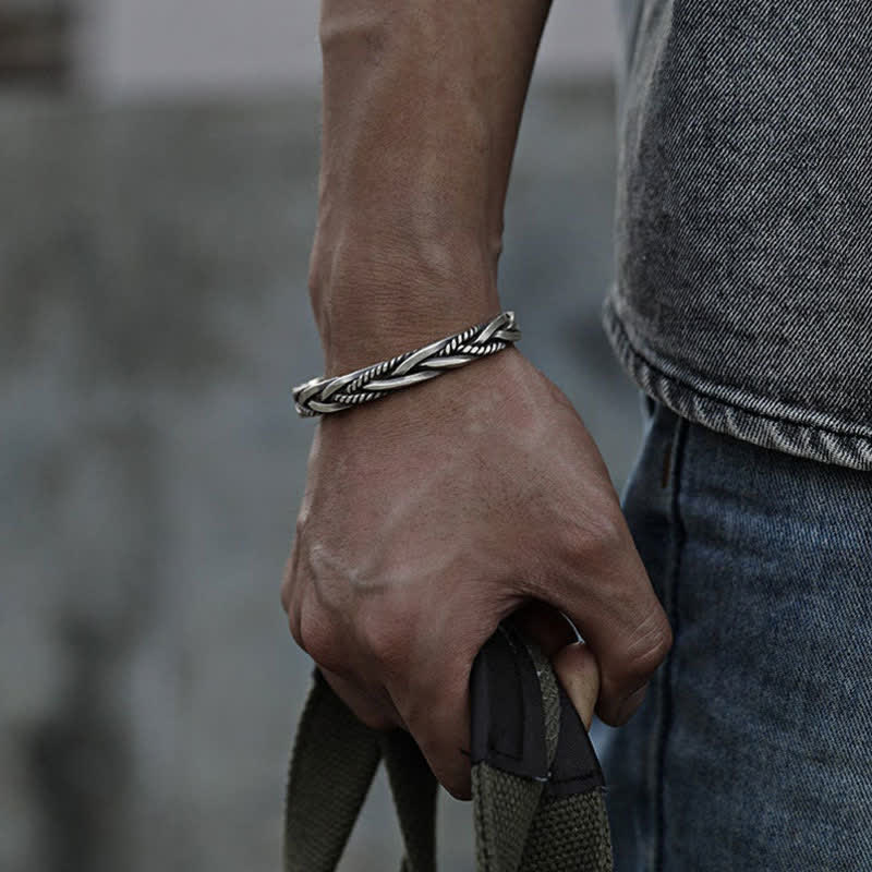 Men's multi-strand twisted silver cuff bracelet with alternating smooth and rope-textured bands oxidized finish worn with gray t-shirt and canvas bag strap