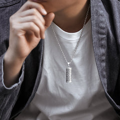 Om Mani Padme Hum Silver Protection Necklace – Polished silver cable chain necklace with ornate barrel pendant featuring scrollwork patterns, styled on model in white crew neck and charcoal blazer