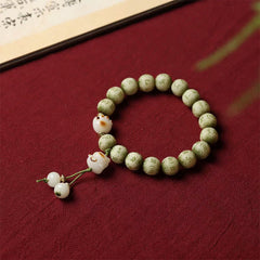 Bodhi Seed Bracelet – Green carved beads with cat paw charm on burgundy fabric beside calligraphy scroll, cat jewelry