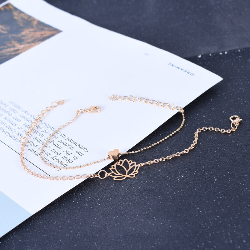 Lotus Heart Enlightenment Bracelet - Rose gold lotus and heart anklet on dark speckled surface, purity jewelry