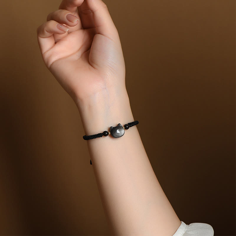 Dainty black woven bracelet with polished gray cat silhouette charm and gold accent beads worn on wrist, adjustable cat protection jewelry