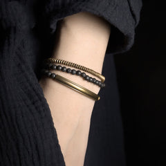 Lava Rock Copper Healing Bracelet – Matte black lava beads with copper wire-wrapped center and silver accents on gray pebbled stone surface, overhead three-quarter