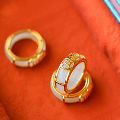 White Jade Luck Ring Necklace – White jade band rings with gold settings featuring Chinese coin prosperity motifs displayed on vermillion silk fabric