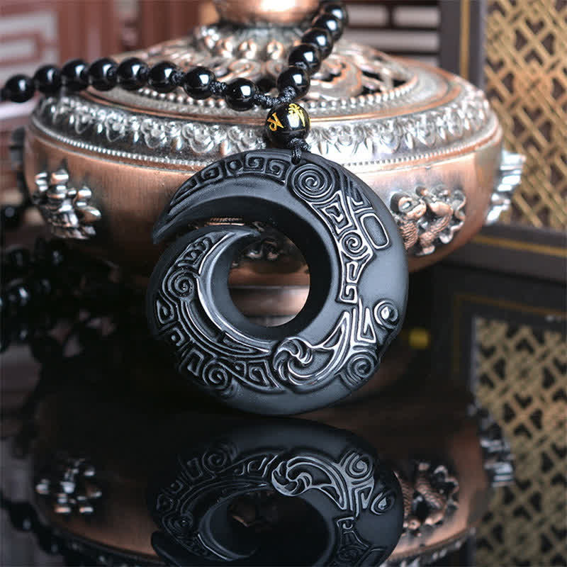 Black Obsidian Ice Obsidian Pendant Necklace – Carved black obsidian spiral medallion with circular cutout and traditional relief patterns, gold character blessing bead, displayed on polished black reflective surface with bronze incense burner and Chinese lattice screen backdrop, spiritual amulet necklace