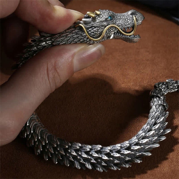 Dragon bracelet held in hand showing oxidized silver scale texture gold accents and detailed dragon head against warm brown background