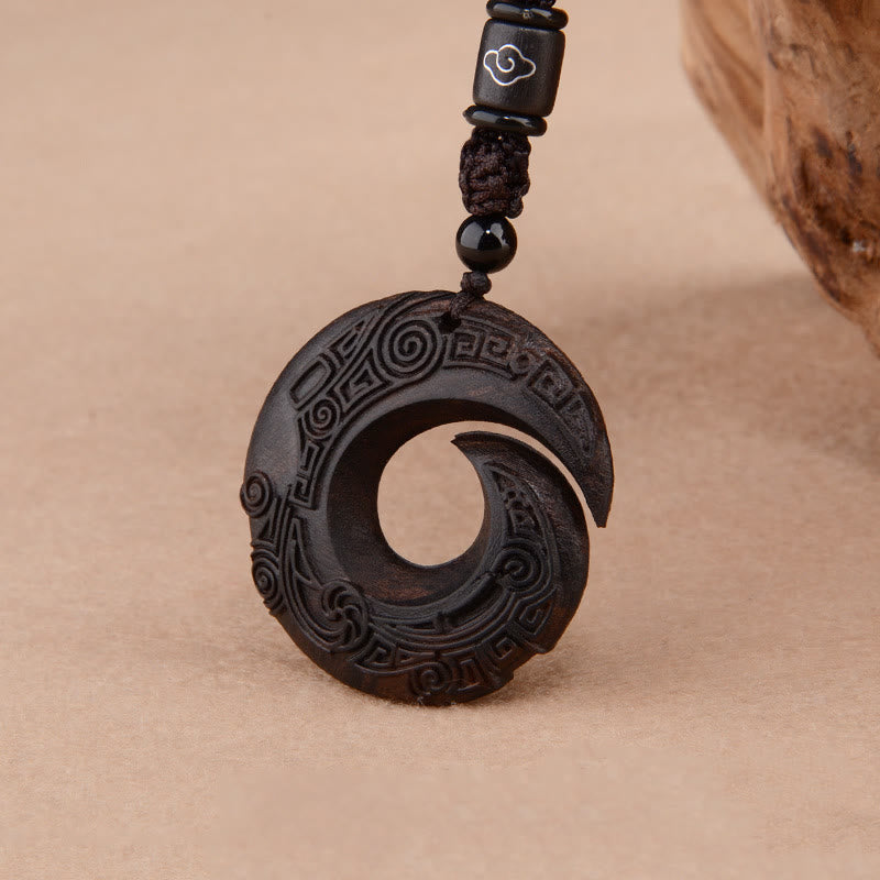 Ebony wood peace buckle pendant with carved spiral bi-disc design showing traditional Chinese ruyi cloud and leiwen key-fret patterns on black hardwood with adjustable black cord