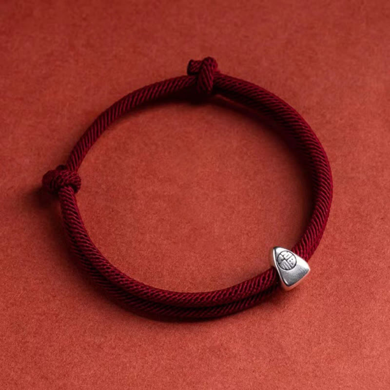 925 Silver Fu Character Braided Bracelet – Burgundy twisted double-strand cord with silver fortune charm on textured red fabric, overhead diagonal angle