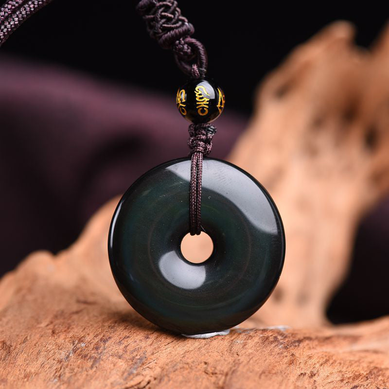 Rainbow obsidian ping'an kou protection necklace with iridescent green-blue sheen and gold-inscribed mantra accent bead on dark braided cord displayed on natural wood