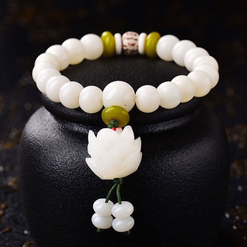 White Bodhi Seed Luck Bracelet – Close-up of lotus carving with green cord and beaded tassel on dark display