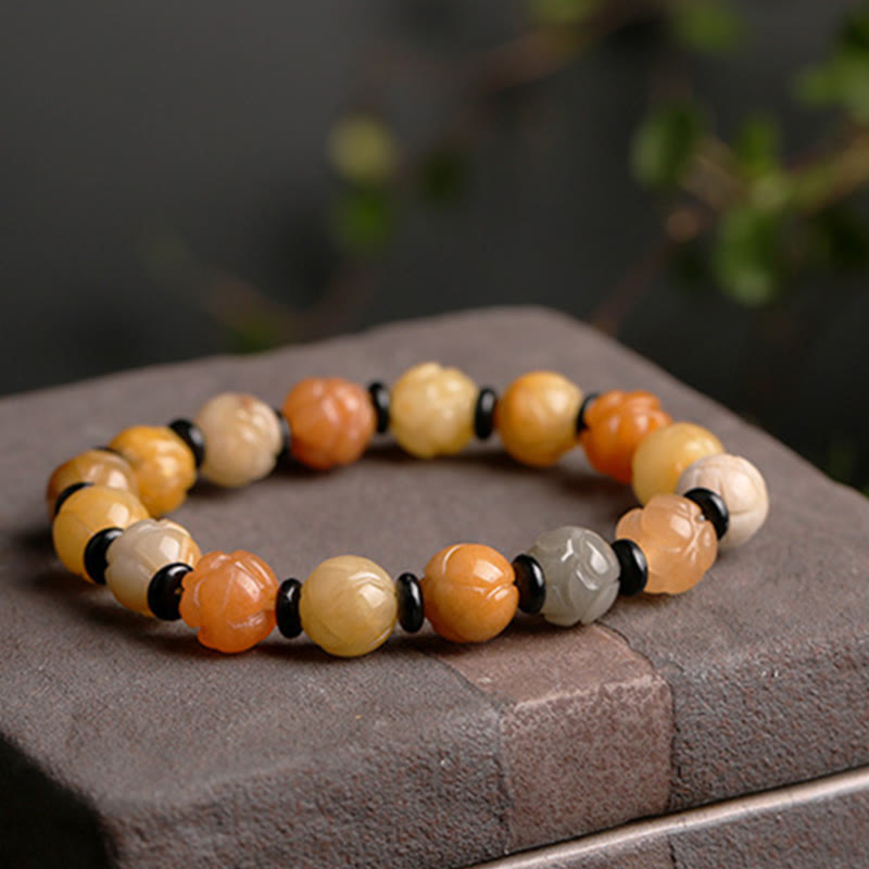 Golden Silk Jade Lotus Bracelet – Warm amber lotus beads with black spacers on dark stone pedestal, lotus wealth jade