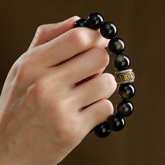 Gold Sheen Obsidian Pixiu Bracelet – hand holding close-up of gold sheen obsidian and bronze om mani padme hum spacer