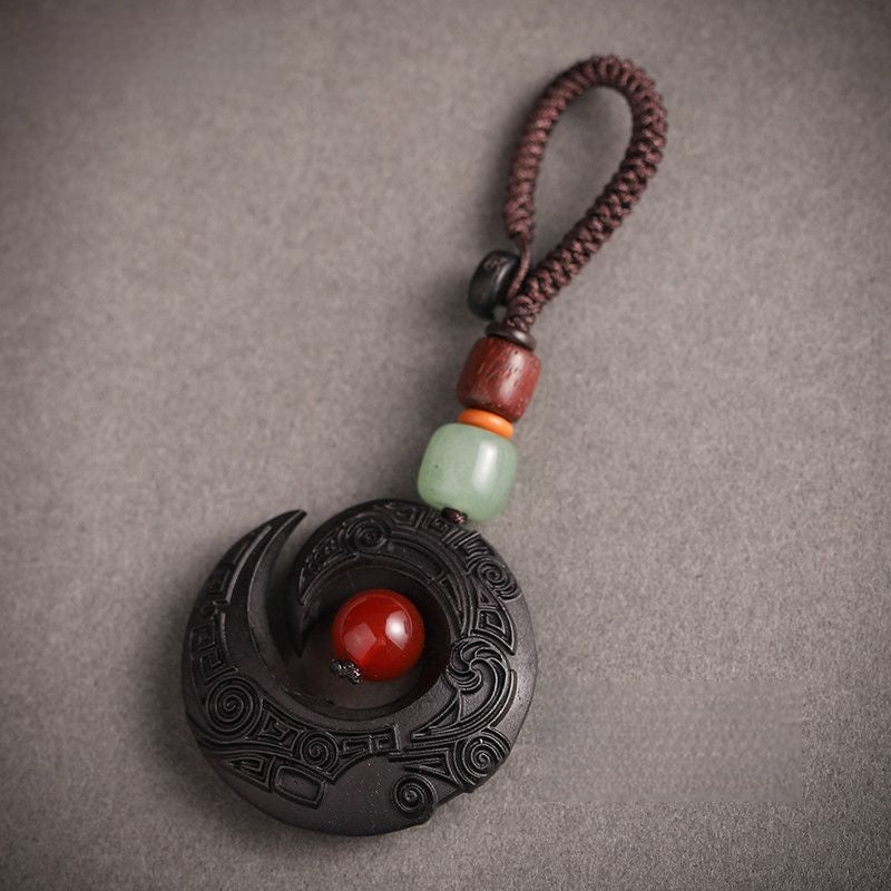 Feng Shui ebony wood protection keychain spiral crescent design with red agate bead on white background