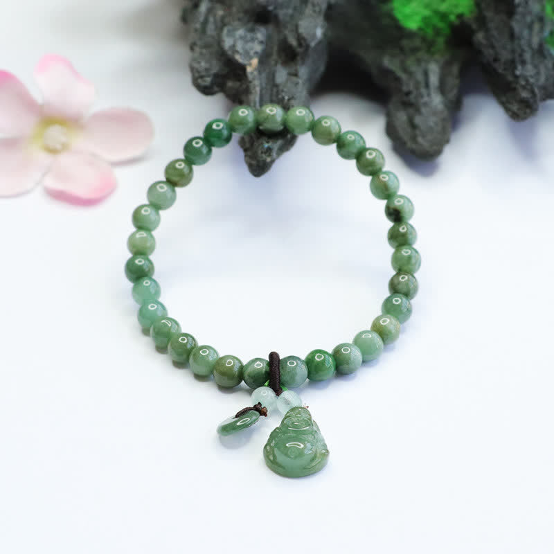 Natural cyan jade bead bracelet with carved green stone Buddha pendant and bi disc charm on white surface with dark rock and pink cherry blossom styling