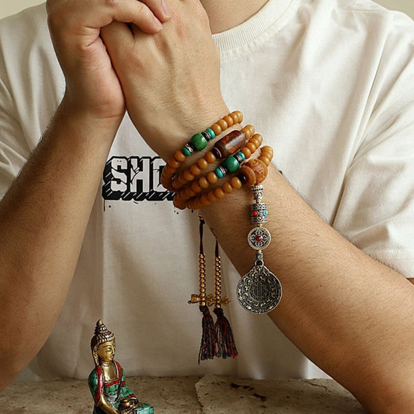 108 Bodhi Seed Mala Bracelet – Multi-wrap bracelet on wrist with tassels beside Buddha statue