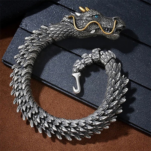 Dragon bracelet with articulated scales and hook clasp on dark leather surface featuring antiqued silver finish gold whiskers and striking blue gemstone eye detail