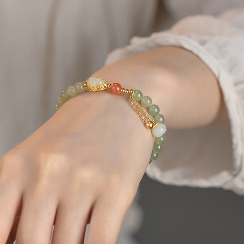 Jade Gourd Lotus Bracelet on wrist with lace sleeve, warm gray bokeh background, flowing chain tassel detail