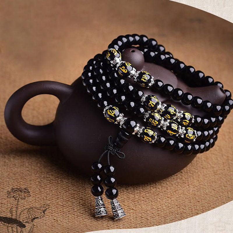 Black Obsidian Mala Bracelet - Coiled on dark clay teapot with gold mantra beads and tassel, obsidian spiritual jewelry