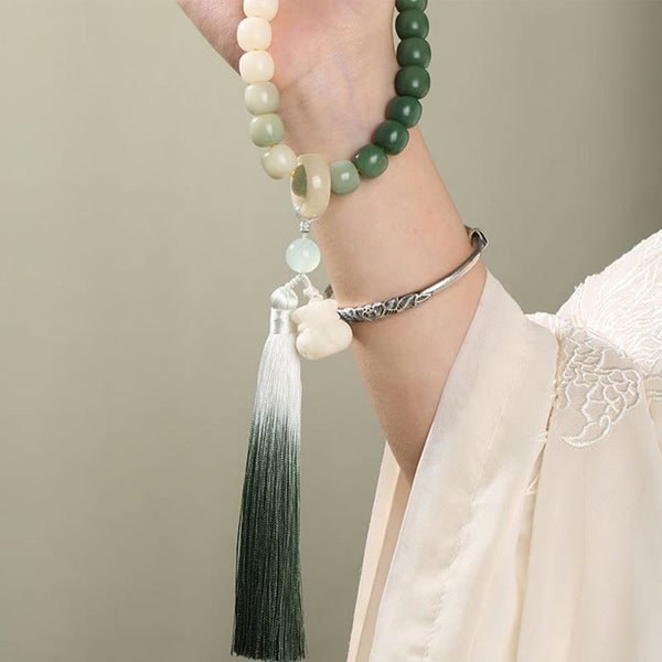 Bodhi Seed Lotus Wisdom Wrist Mala – Prayer bead bracelet worn on raised hand in Hanfu, ombre green tassel flowing, zen aesthetic