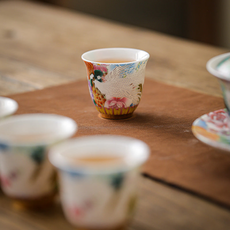 Dragon Phoenix Ceramic Teacup - Cup with amber tea beside blurred gaiwan on leather mat, Serene ritual