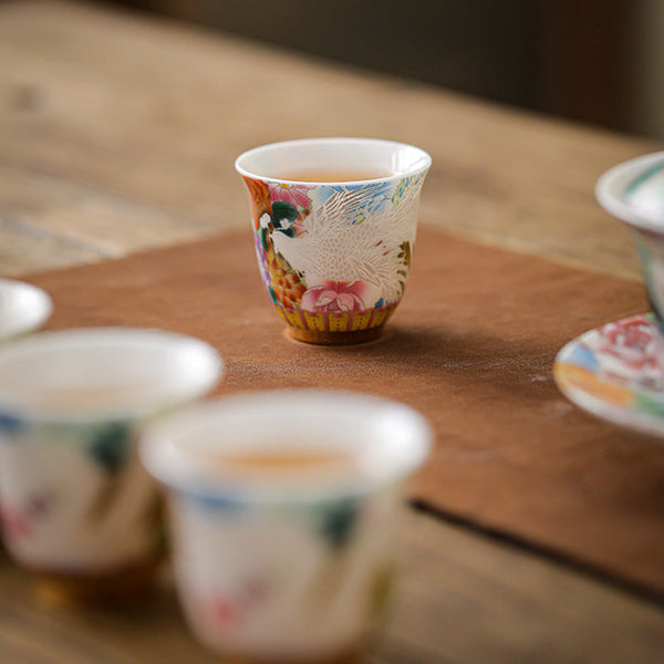 Dragon Phoenix Ceramic Teacup - Cup with amber tea beside blurred gaiwan on leather mat, Serene ritual
