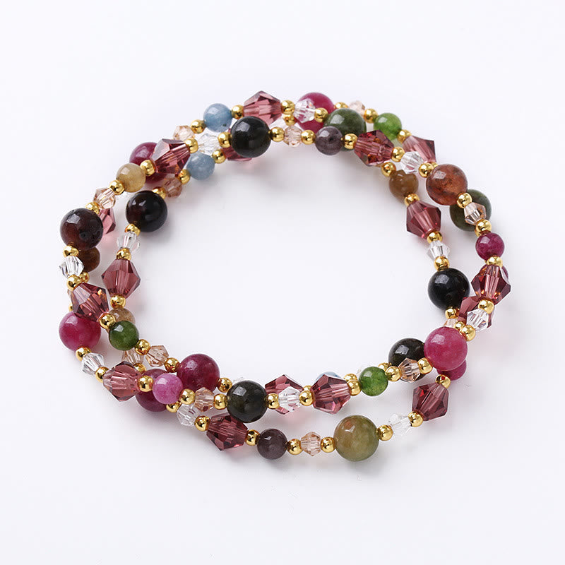 Triple-strand multi-color tourmaline bracelet coiled on white background, featuring green black pink and amber gemstone beads with purple crystal and gold accents