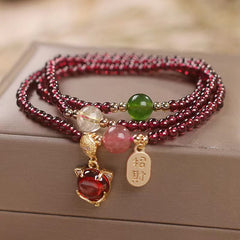 Triple-strand garnet bracelet with fox face charm red cabochon gemstone zhao cai wealth invitation gold tag and mixed semi-precious accent beads on taupe display surface