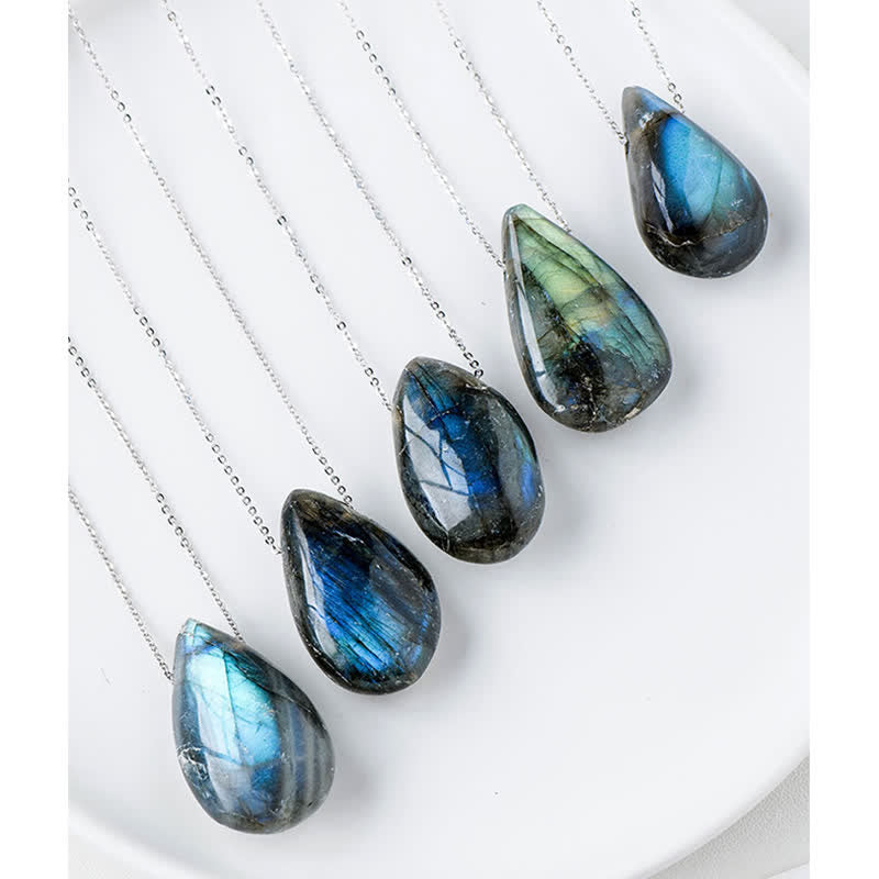Labradorite water drop pendant necklace set of five teardrop labradorite cabochons with dominant blue and cyan iridescent flash on silver chains arranged in white porcelain dish