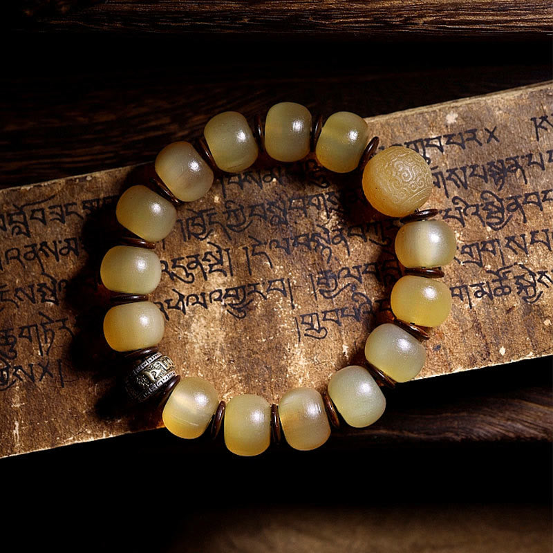 Tibetan Sheep Horn Skull Bracelet – Flat lay on aged manuscript, carved mantra bead and metal charm