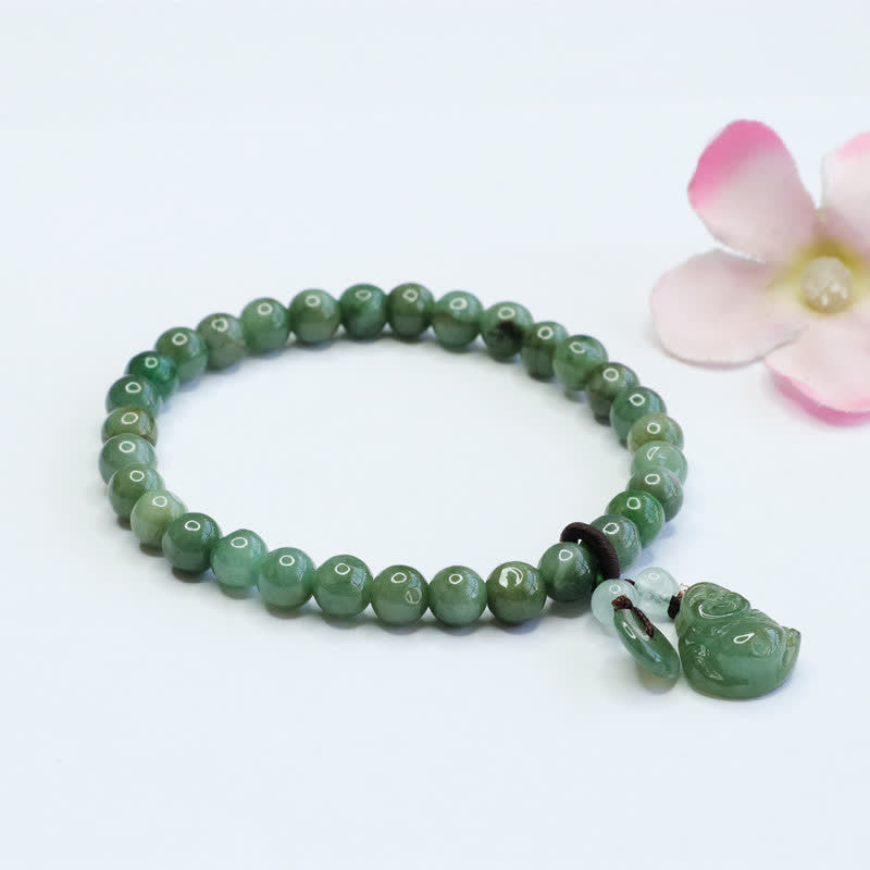 Cyan jade bead bracelet with carved green stone pendant charm and white jade spacer beads on clean white surface with soft pink flower accent