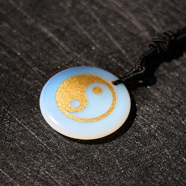 Yin Yang Crystal Necklace – Round opalite pendant with gold textured yin-yang design, iridescent white-blue stone on black co