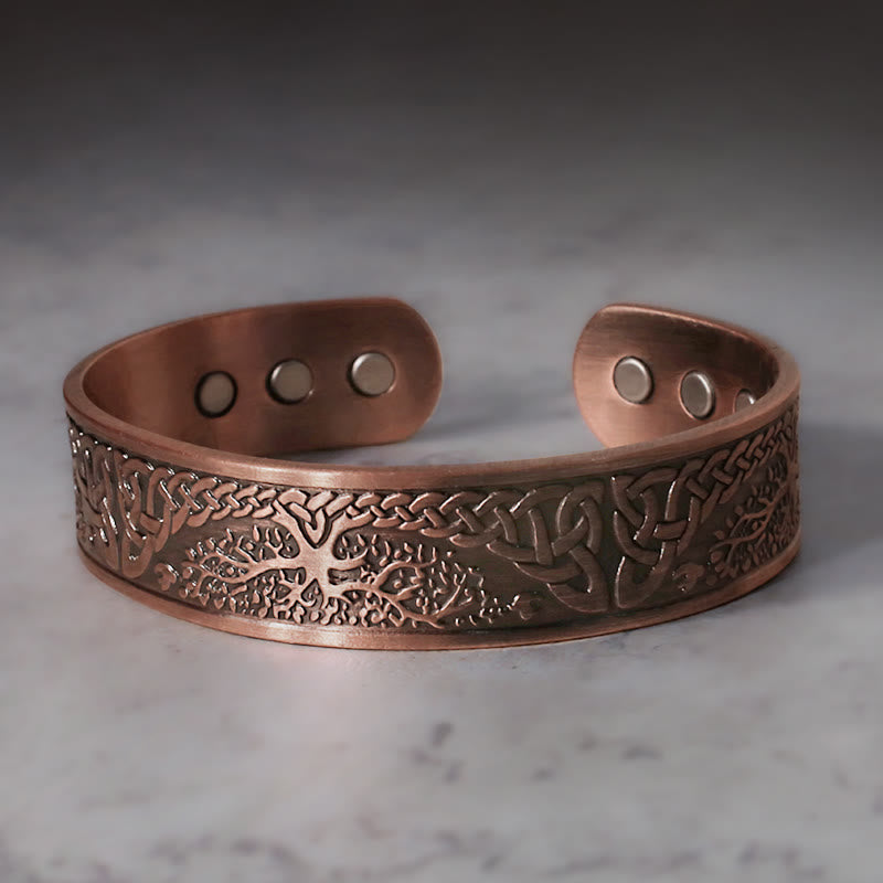 Tree of life copper magnetic cuff bracelet with Celtic knotwork engraving and six interior therapy magnets on light marble background