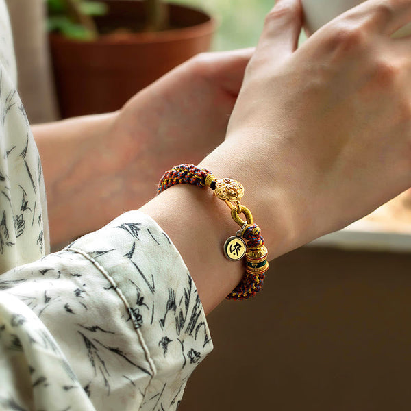 Om Mani Padme Hum Braided Bracelet – Worn on wrist showing braided cord and gold mantra charm with intricate weave detail