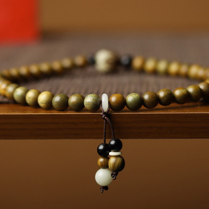 Green Sandalwood Lotus Bracelet – side view on wooden ledge, tassel with cream terminal bead