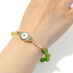 Peridot green bead bracelet with crystal evil eye charm worn on wrist, white background
