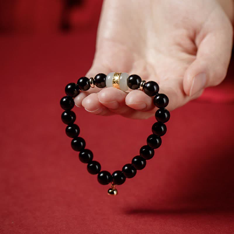 Black Obsidian Jade Bracelet – Held in open palm showing full loop with gold bell charm, red backdrop