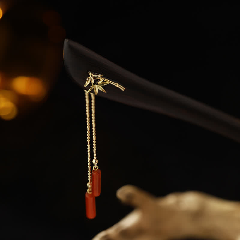 Dramatic dark background shot of ebony hairpin with gold bamboo inlay and dangling red agate tassels