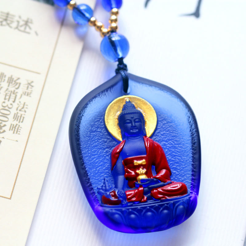 Liuli Crystal Medicine Buddha Pendant – blue liuli with gold halo resting on book with beaded chain, detail